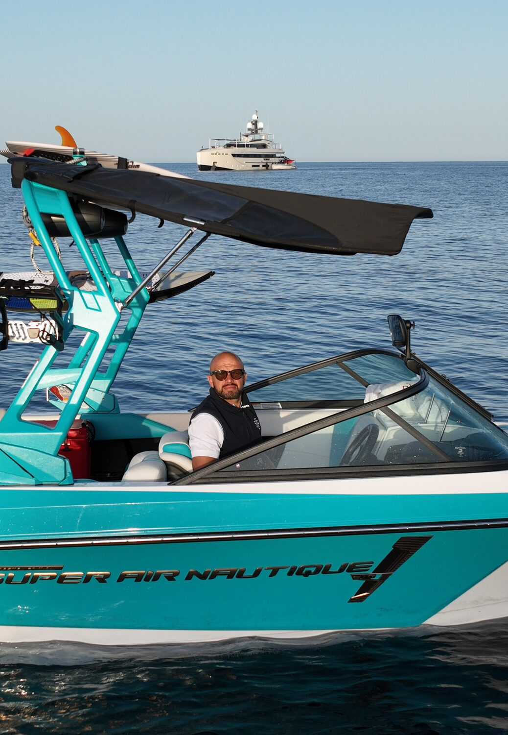 Coach at the helm of a wake tender with a superyacht at anchor